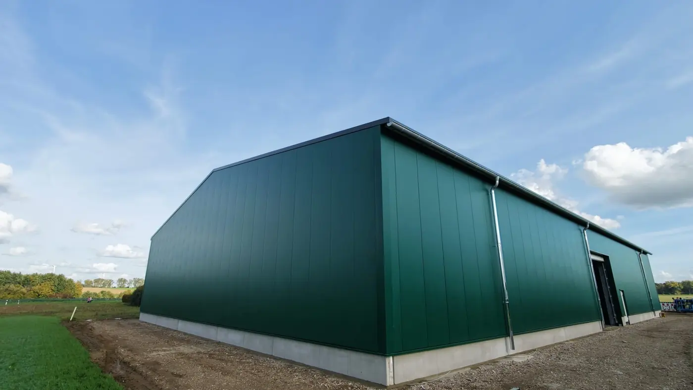 Giebelwand und Längsseite einer Halle mit grünen Profilpaneelen und Dachrinne