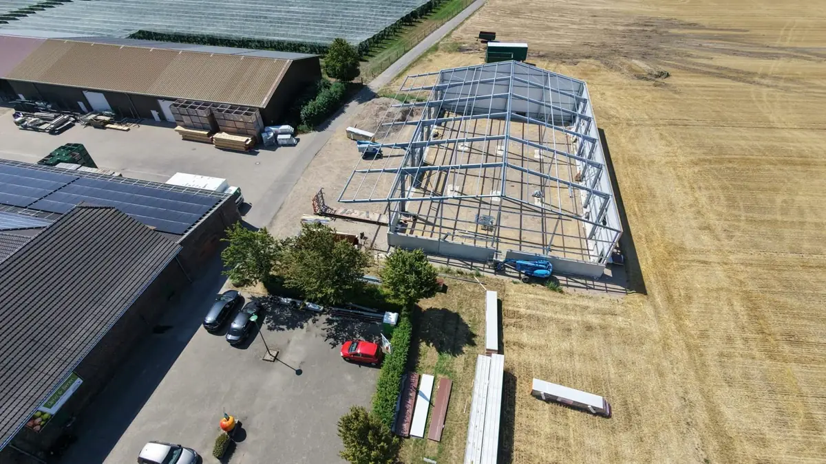 Hallenmontage aus der Luft – offene Stahlkonstruktion einer Halle mit ersten Wandelementen