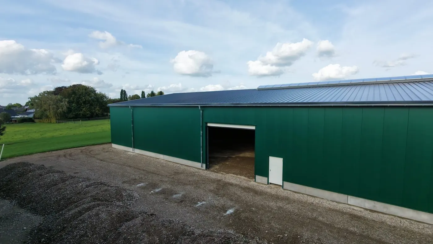 Längsseite einer fertigen Halle mit grünen Wandpaneelen, Toreinfahrt und Fallrohr